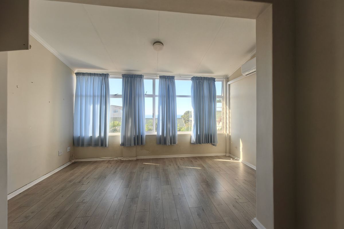 A bright, empty living room featuring laminate flooring, a split-system air conditioner, and large windows with natural light.