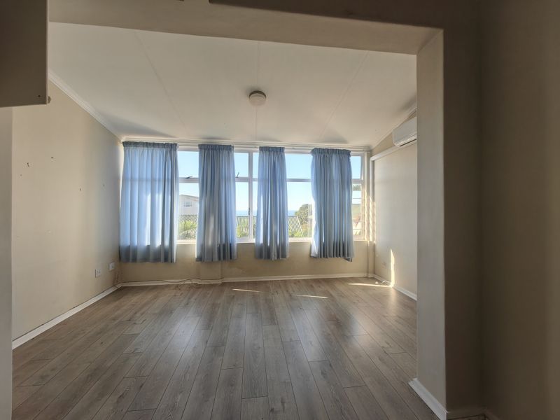 A bright, empty living room featuring laminate flooring, a split-system air conditioner, and large windows with natural light.