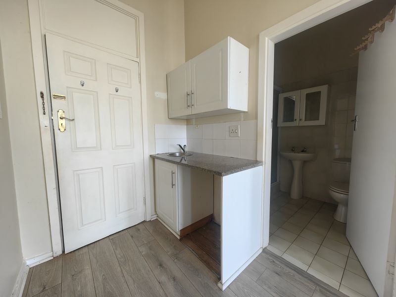 A compact kitchenette area featuring a small sink, granite countertop, and built-in cabinetry, adjacent to a tiled bathroom entrance.