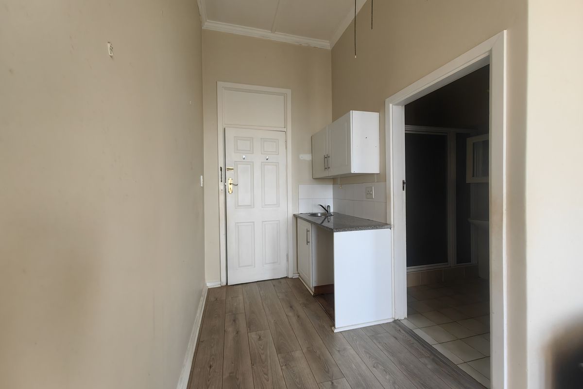 A compact kitchenette area featuring basic cabinetry, a sink, and laminate flooring, leading into an adjacent bathroom space.