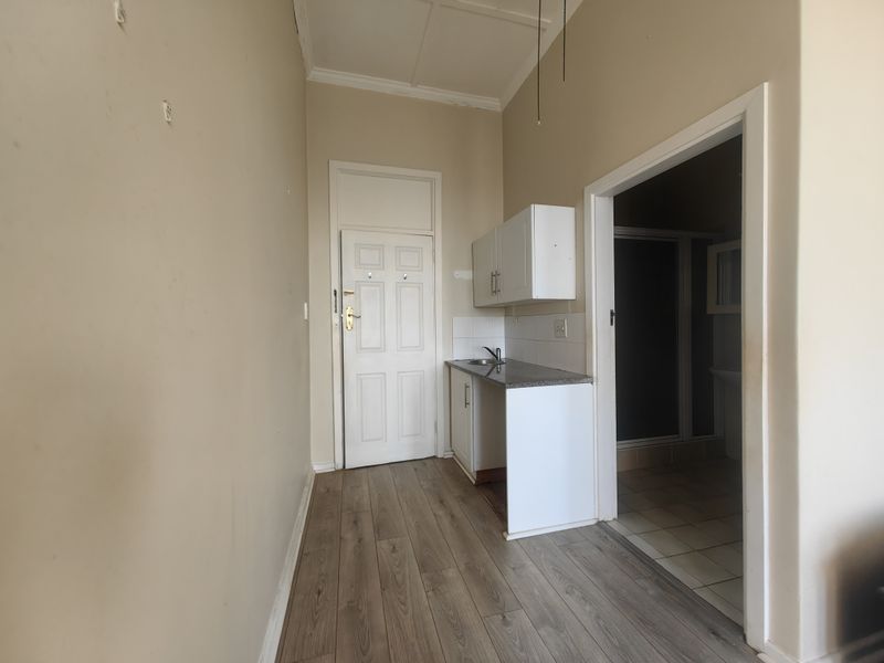 A compact kitchenette area featuring basic cabinetry, a sink, and laminate flooring, leading into an adjacent bathroom space.