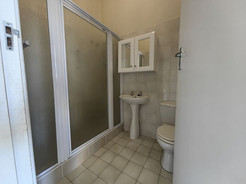 A functional bathroom featuring a shower enclosure, pedestal basin, wall-mounted medicine cabinet, and neutral ceramic tiling throughout.