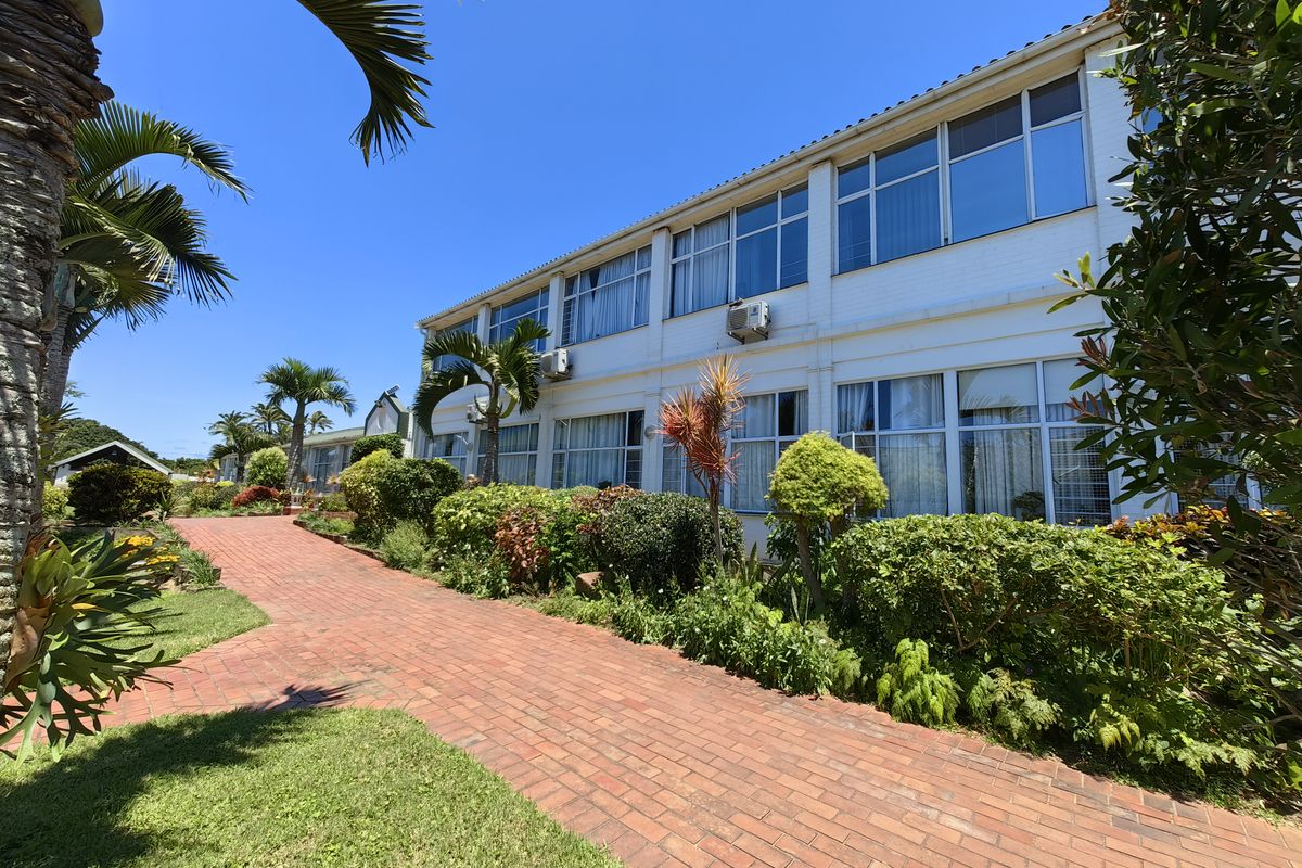 A well-maintained exterior view of a retirement village building featuring a brick pathway, landscaped gardens, and large windows across multiple levels.