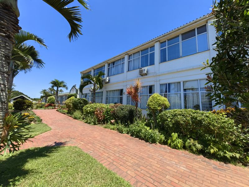 A well-maintained exterior view of a retirement village building featuring a brick pathway, landscaped gardens, and large windows across multiple levels.