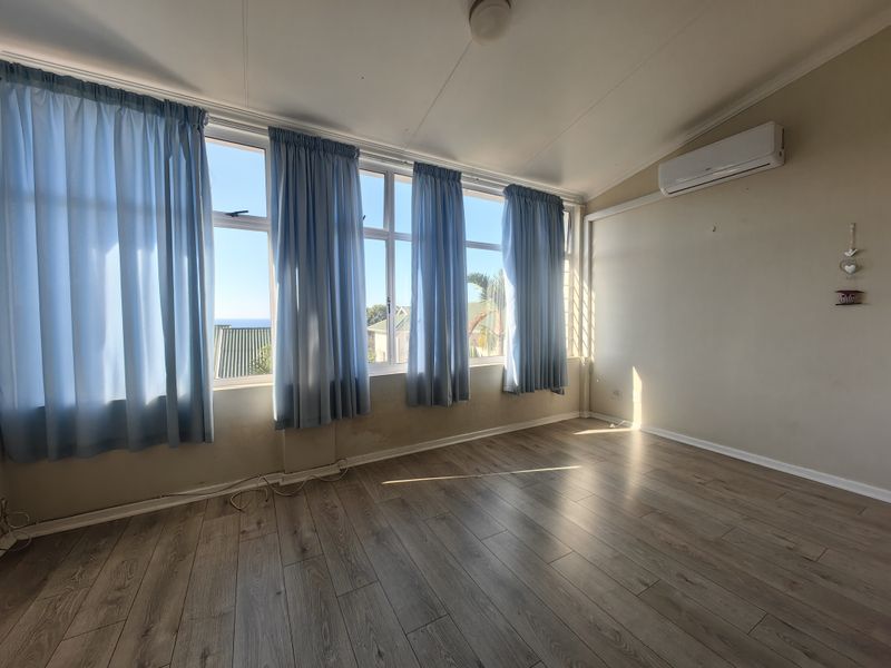 Bright, empty living area featuring laminate flooring, a wall-mounted air conditioning unit, and large windows with natural light.