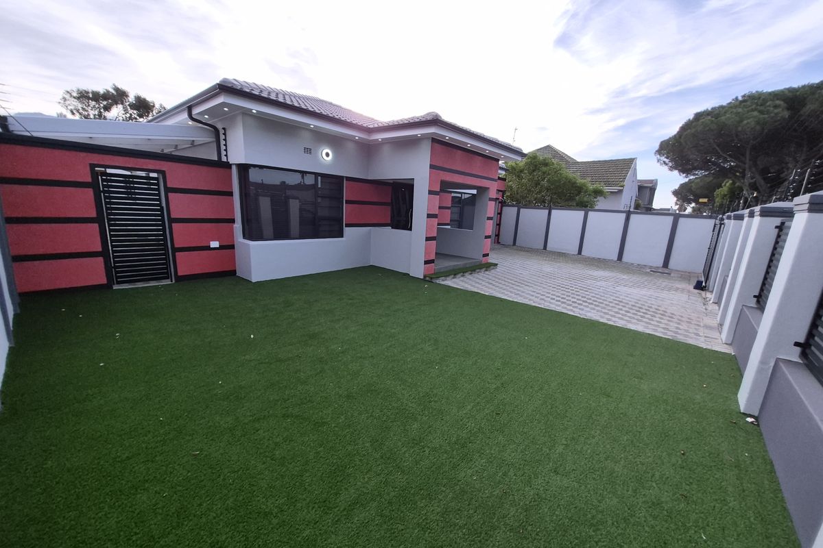 A well-maintained rear exterior featuring artificial turf, a paved driveway, and a secure perimeter wall with modern lighting.