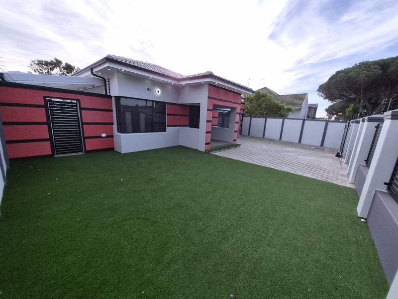 A well-maintained rear exterior featuring artificial turf, a paved driveway, and a secure perimeter wall with modern lighting.