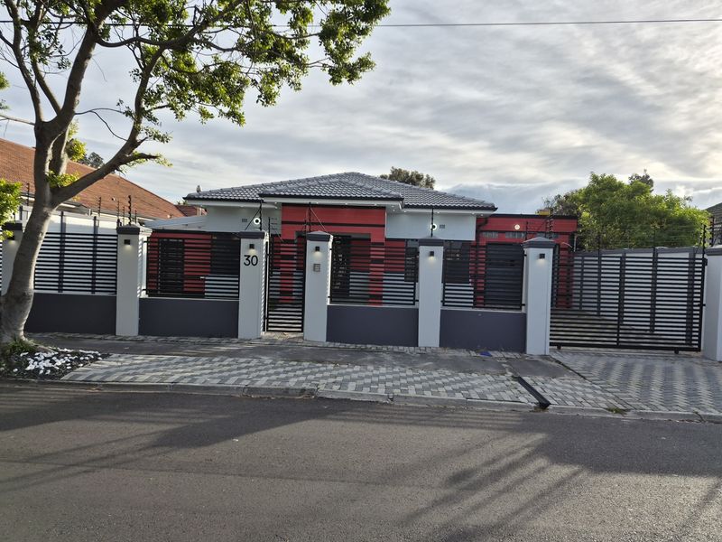 Front elevation of a modern house featuring a secure perimeter wall, electric fencing, sliding gate, and paved driveway.
