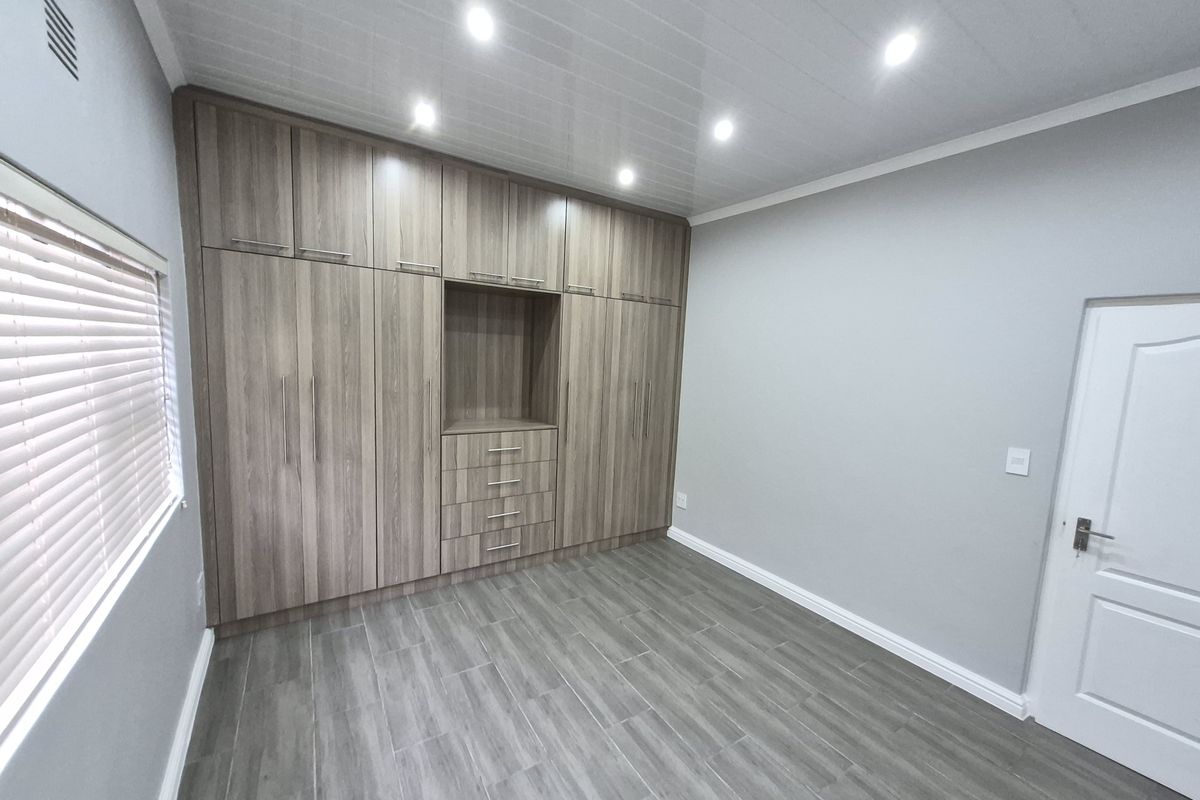 A clean, modern bedroom featuring extensive built-in wooden cabinetry, tiled flooring, recessed lighting, and neutral wall finishes.
