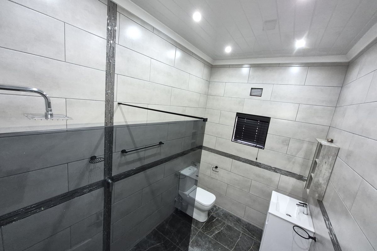 Modern bathroom featuring a spacious walk-in shower with a rain shower head, contemporary vanity, and stylish floor-to-ceiling tiling.