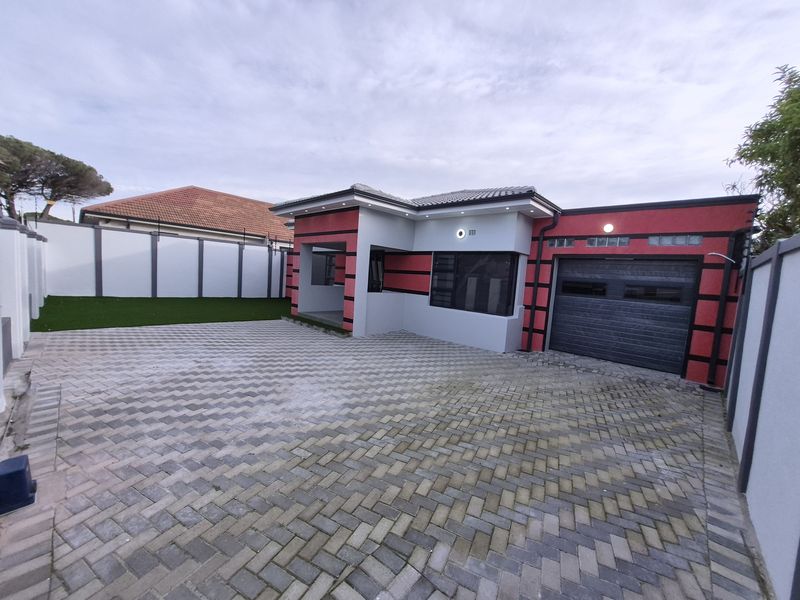 Modern front elevation featuring a paved driveway, single garage, and secure boundary walls with artificial lawn area.