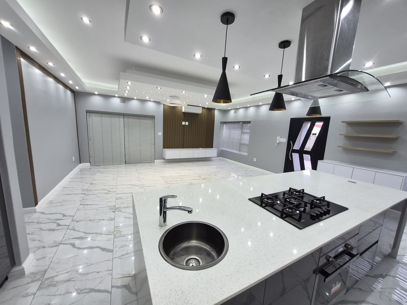 Modern open-plan living and kitchen area featuring a large island with gas hob, sleek cabinetry, recessed lighting, and high-quality marble-look tiled flooring.
