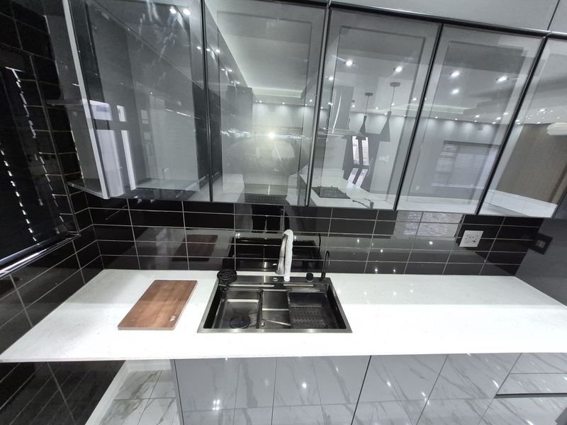 Modern kitchen featuring high-gloss cabinetry, a sleek quartz countertop, black subway tile backsplash, and a contemporary undermount sink with integrated lighting.