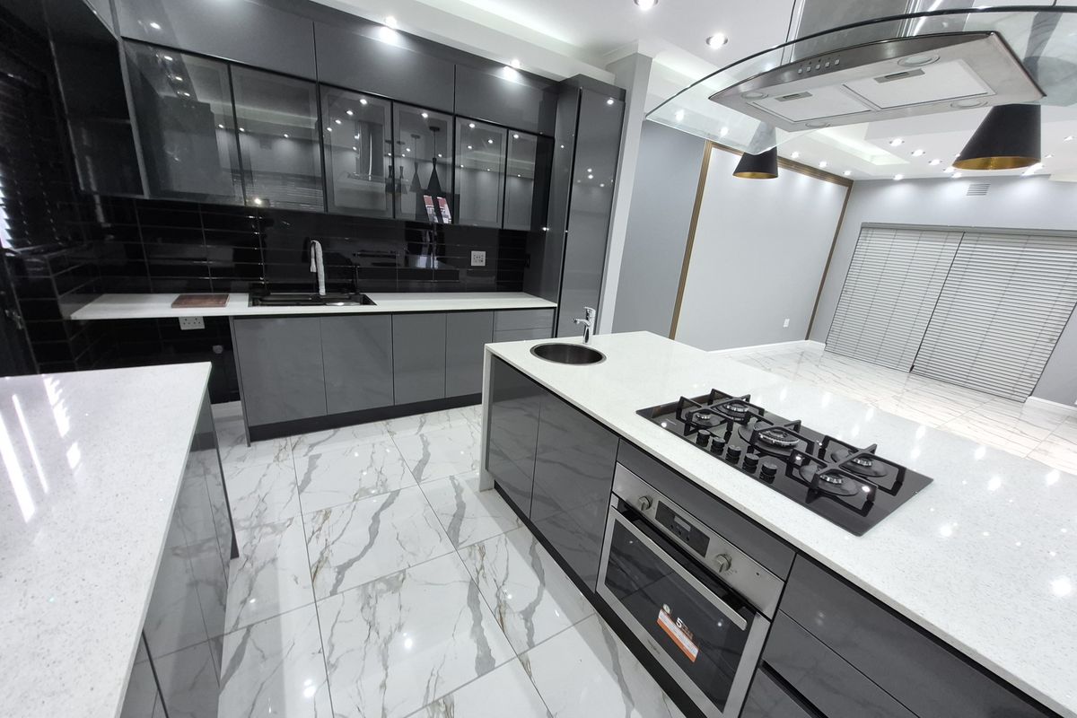 Modern kitchen featuring high-gloss grey cabinetry, quartz countertops, marble-look floor tiles, a central island with a gas hob, and integrated appliances.