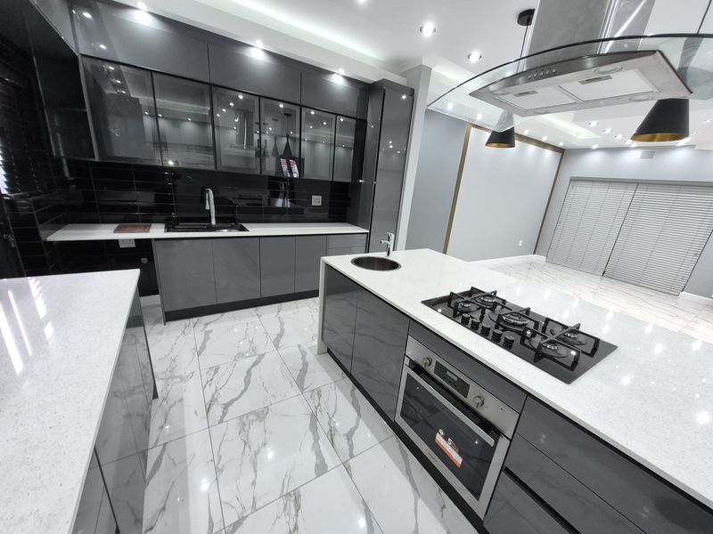 Modern kitchen featuring high-gloss grey cabinetry, quartz countertops, marble-look floor tiles, a central island with a gas hob, and integrated appliances.