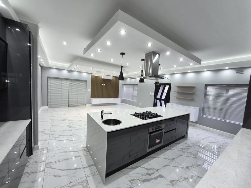 Spacious open-plan kitchen and living area featuring a large central island with gas hob, modern cabinetry, marble-look flooring, and sophisticated recessed ceiling lighting.
