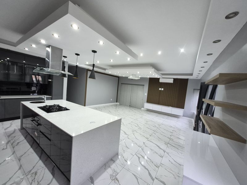 Modern open-plan living and kitchen area featuring a large island with gas cooktop, marble-look tiled flooring, recessed ceiling lighting, and sleek built-in cabinetry.