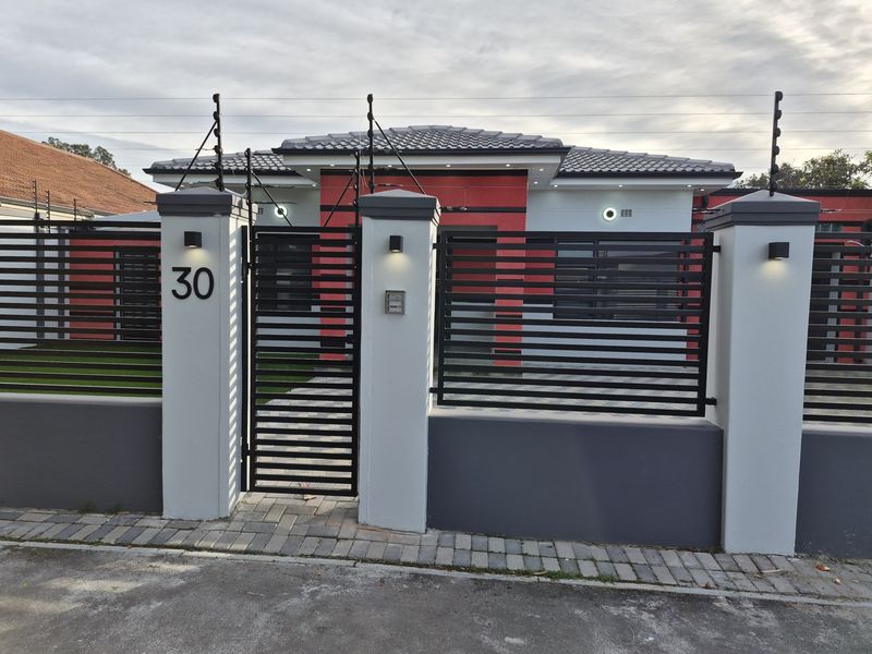 Modern front facade featuring a secure gated entrance, paved driveway, and contemporary exterior lighting with integrated electric fencing.