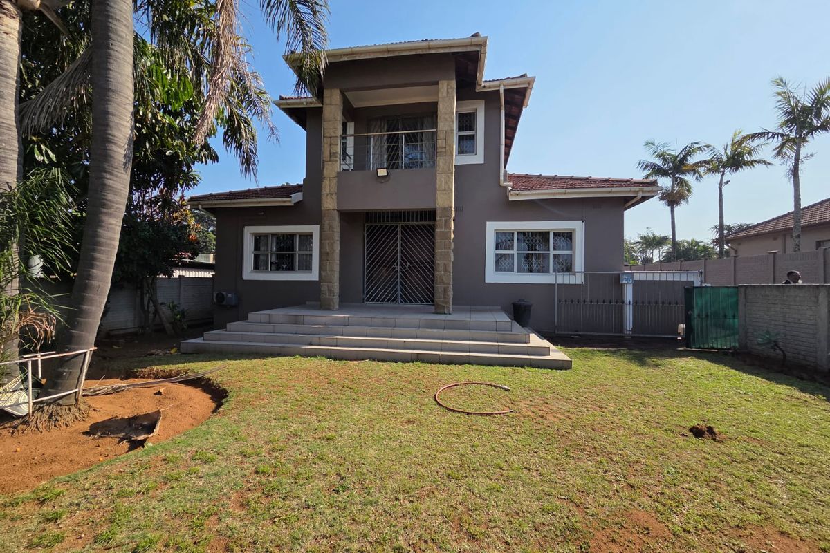 Rear view of a two-story house featuring a tiled patio, stone-clad pillars, a balcony, and a spacious garden area.