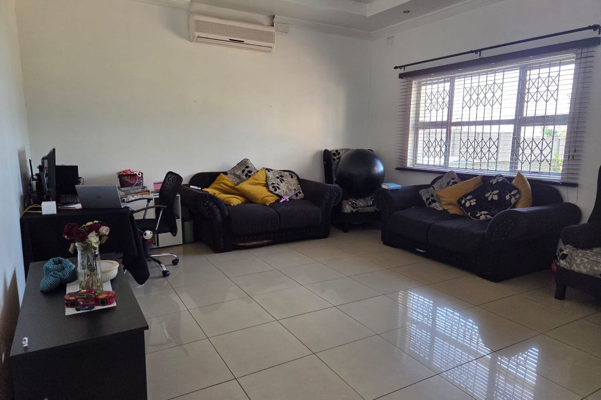 A spacious living room featuring large format floor tiles, a wall-mounted air conditioning unit, and a window fitted with security bars.