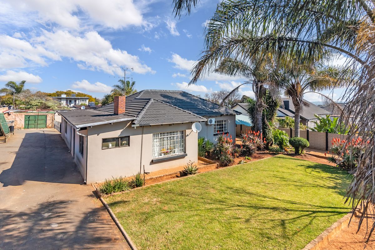 Rear view of the house featuring a tiled roof, brick chimney, paved driveway, and a well-maintained garden area.