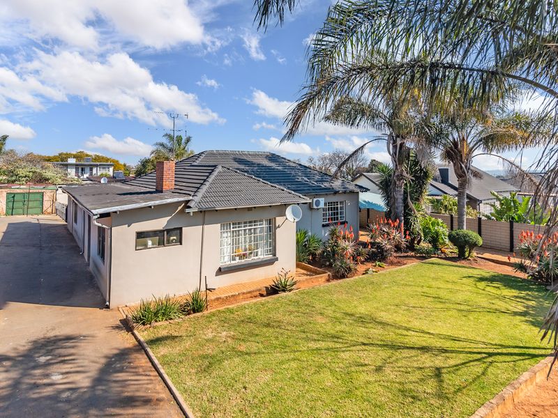 Rear view of the house featuring a tiled roof, brick chimney, paved driveway, and a well-maintained garden area.