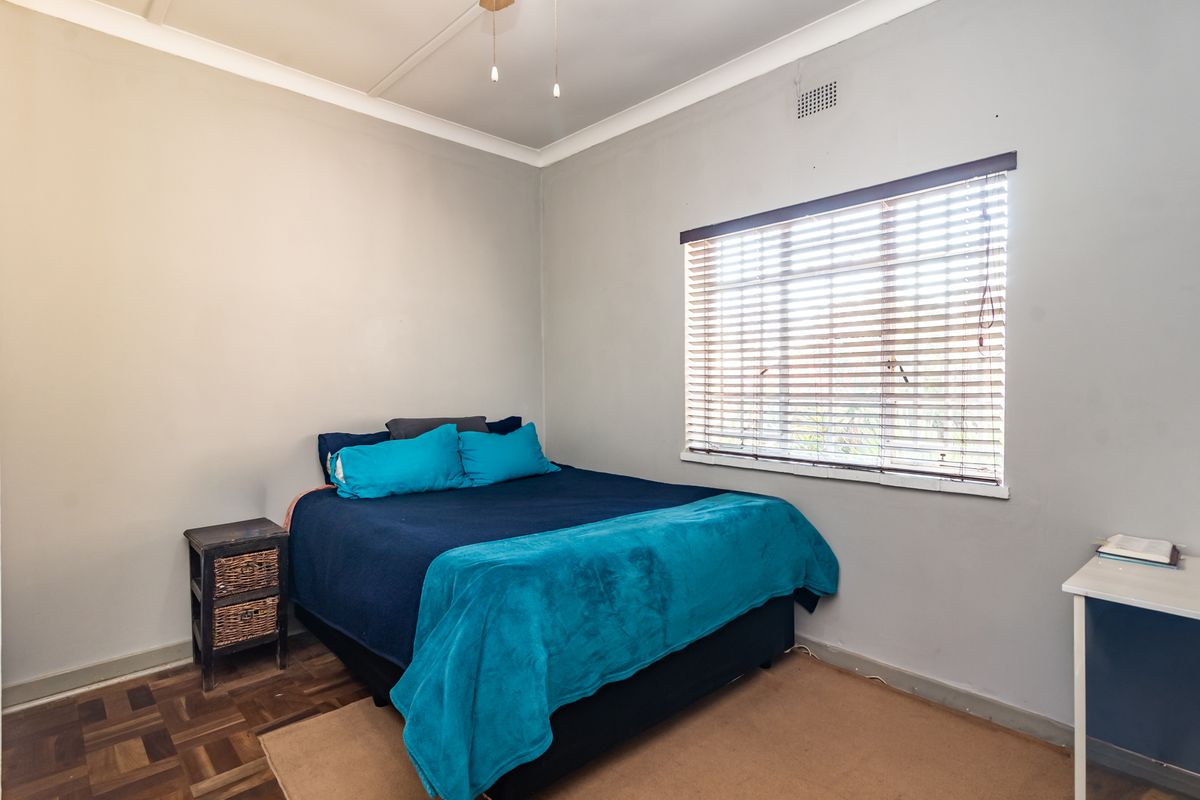 A functional bedroom featuring classic parquet flooring, neutral wall tones, and a window fitted with venetian blinds.