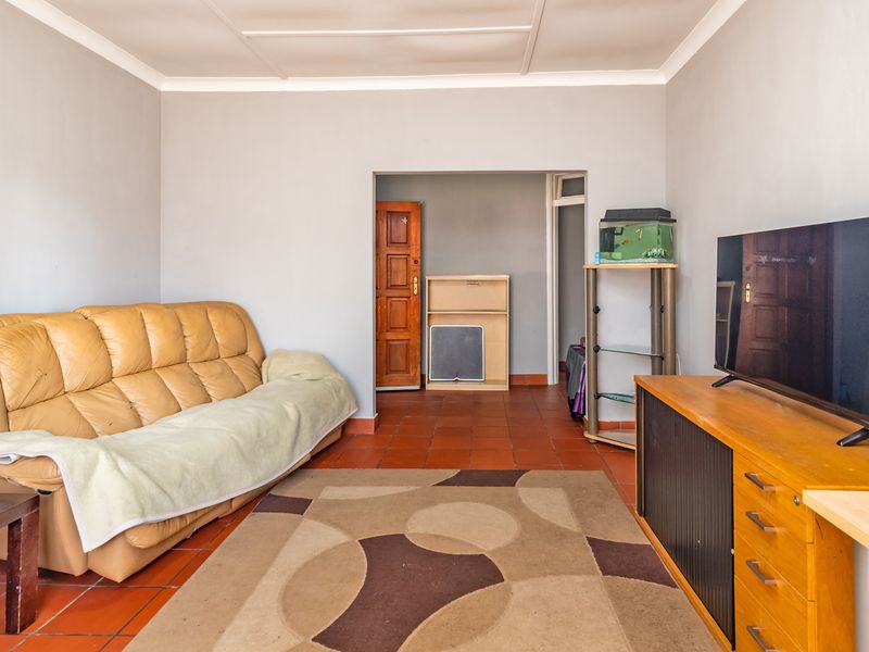 A living room featuring terracotta floor tiles, coved ceilings, and a wooden door leading to an adjacent space.