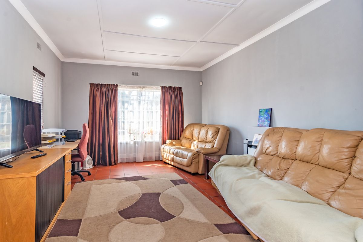 A living room featuring tiled flooring and a coved ceiling, with natural light entering through a window fitted with security bars.