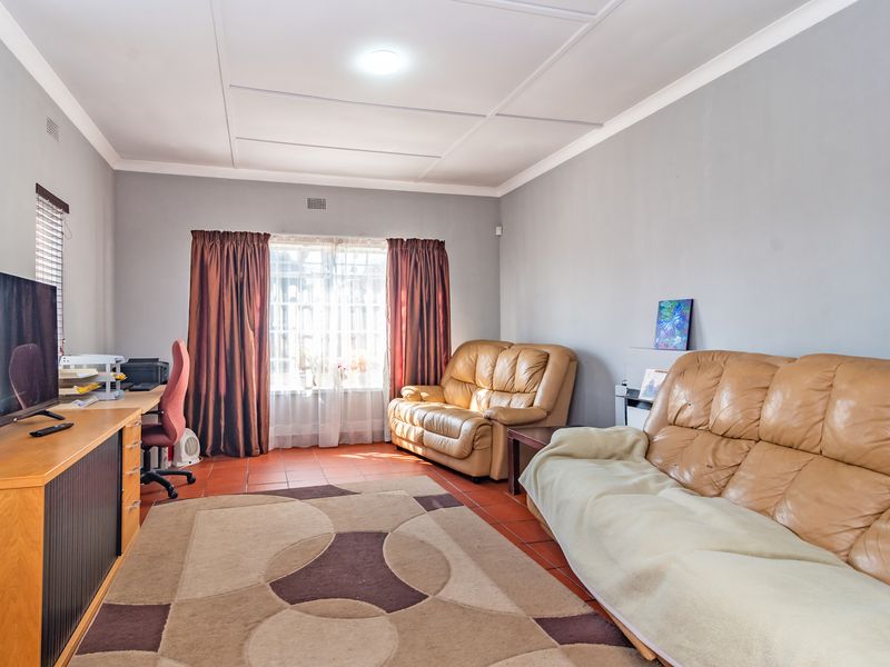 A living room featuring tiled flooring and a coved ceiling, with natural light entering through a window fitted with security bars.