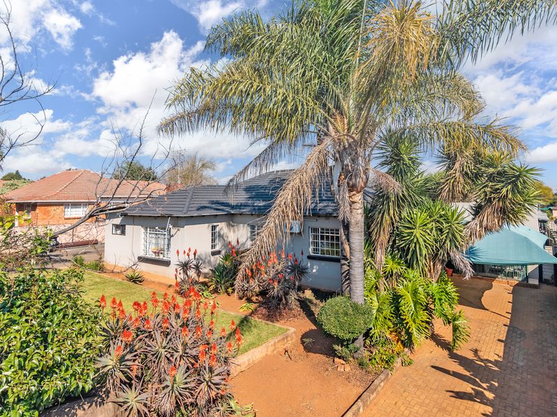 Front view of a single-story house featuring a tiled roof, security bars on windows, a paved driveway, and a well-established garden.
