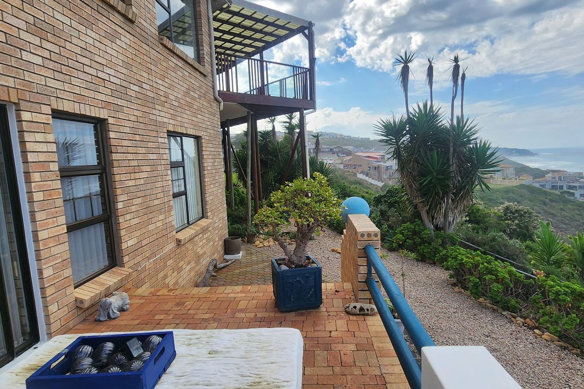 Rear exterior view featuring a brick facade, a raised wooden balcony, and a paved patio area overlooking the coastal landscape.
