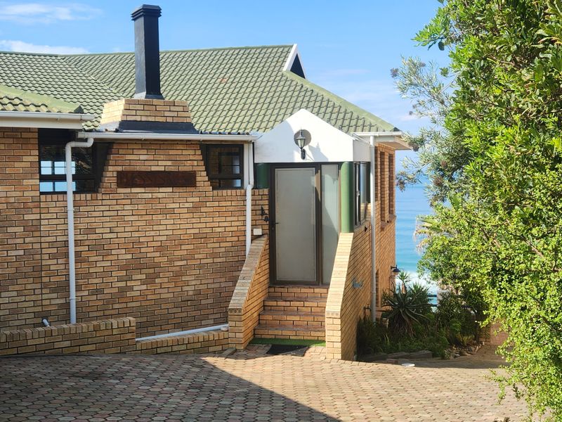 A view of the front exterior of a brick house featuring a tiled roof, chimney, and paved driveway with a glimpse of the ocean.