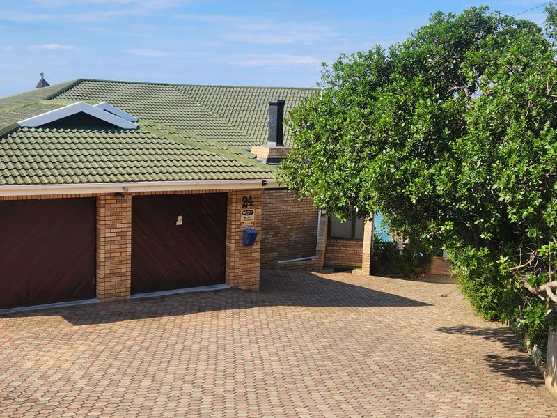 Front exterior view of a brick house featuring a double garage, paved driveway, and tiled roof, situated in a coastal neighborhood.