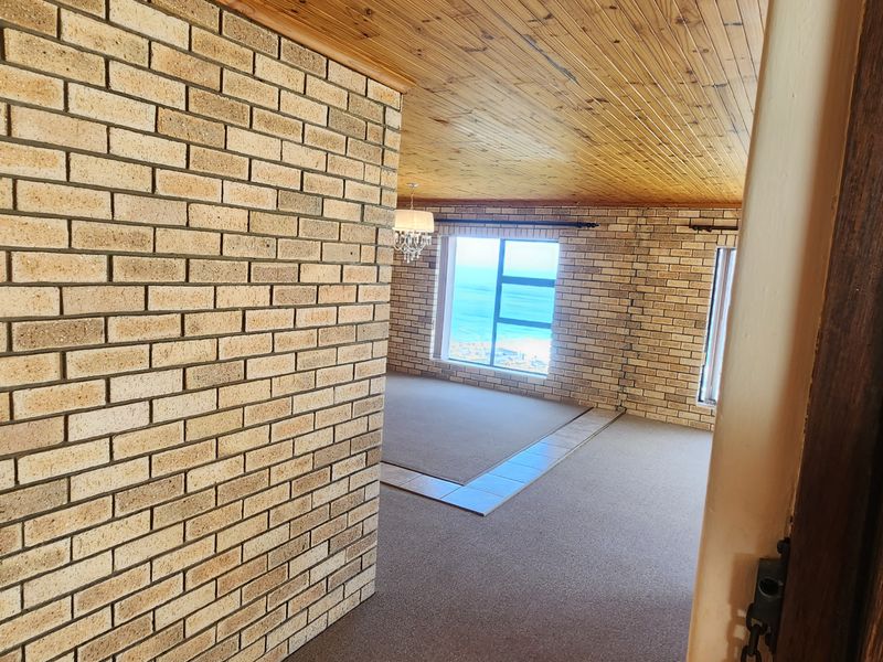 Spacious living area featuring exposed brick walls, timber ceiling, and large windows with ocean views, offering a bright and open atmosphere.