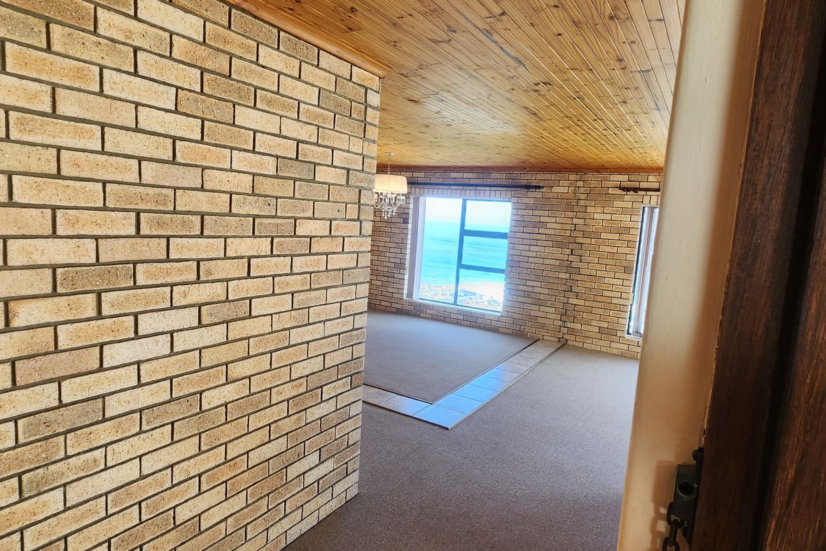 Spacious living area featuring exposed brick walls, timber ceiling, and large windows with ocean views, offering a bright and open atmosphere.