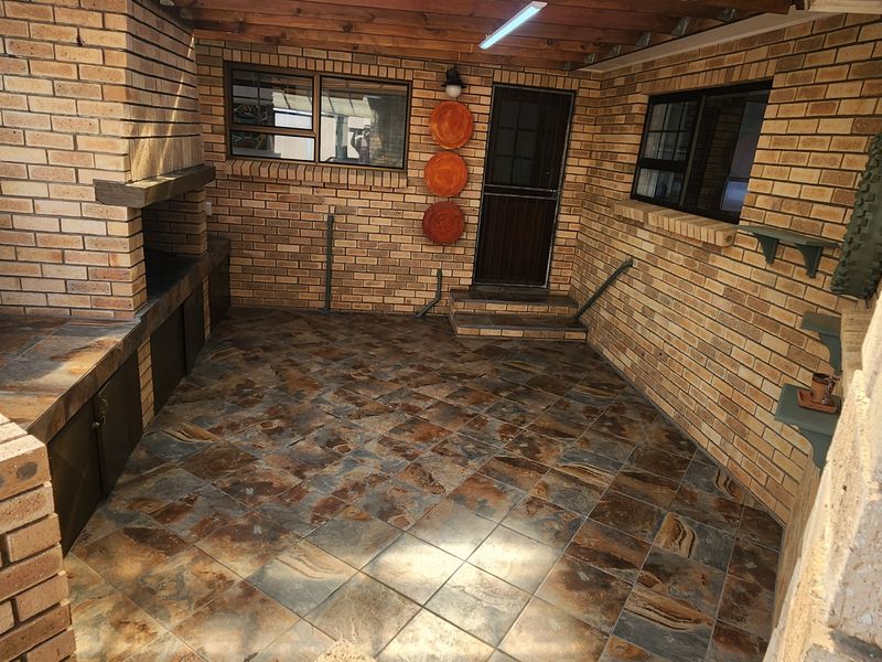 Covered outdoor patio area featuring a built-in brick braai, tiled flooring, and exposed timber ceiling beams, ideal for outdoor entertaining.