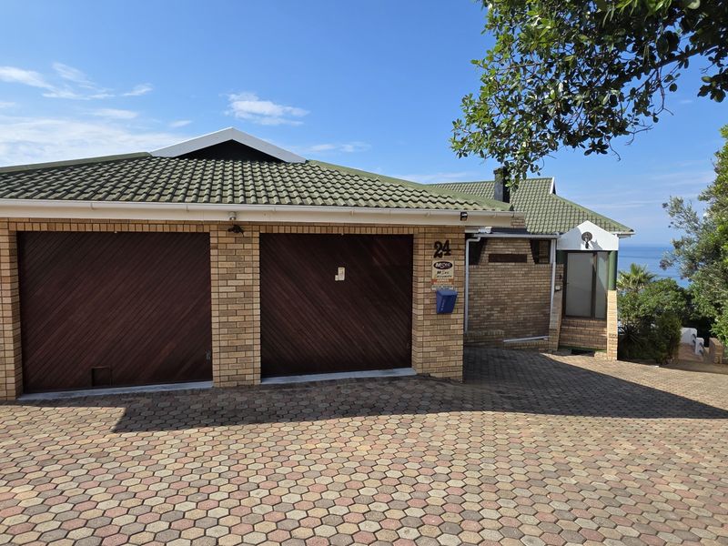 Front exterior view of the property featuring a double garage with timber doors, brick facade, and a paved driveway.