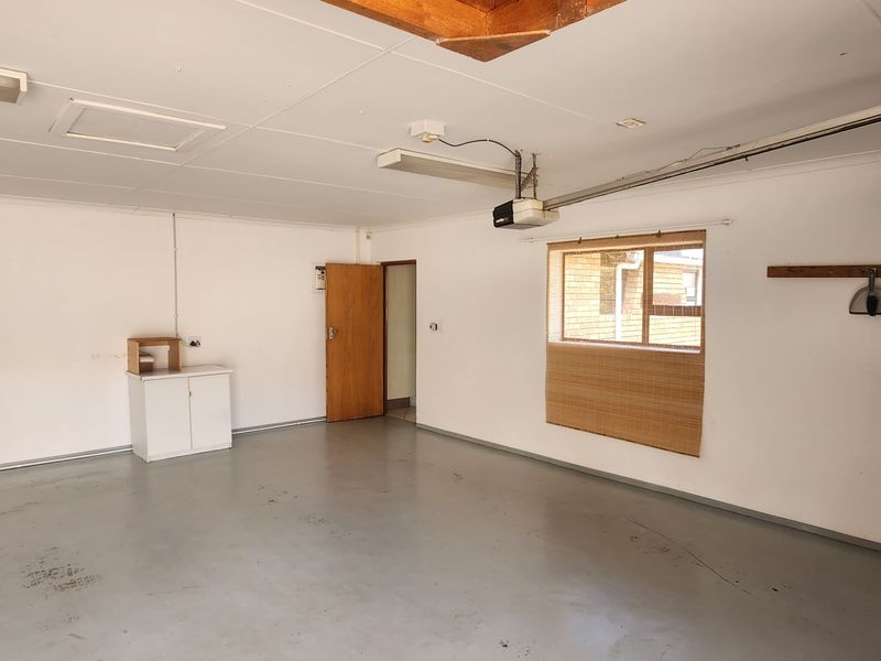 A spacious, clean garage featuring a painted concrete floor, functional lighting, and built-in timber shelving, offering versatile storage or workspace potential.