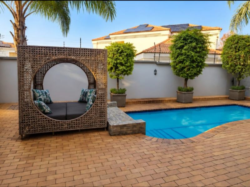 A well-maintained outdoor pool area featuring paved decking, a perimeter wall with electric fencing, and a decorative wall-mounted fountain.