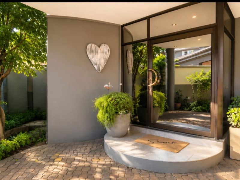 A welcoming front entrance featuring a paved approach, a modern glass door, and a raised concrete step, surrounded by established garden landscaping.
