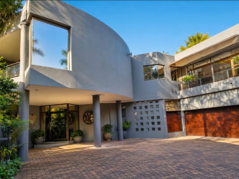 Modern architectural front elevation featuring a curved facade, paved driveway, double garage with timber doors, and a covered entrance with structural columns.
