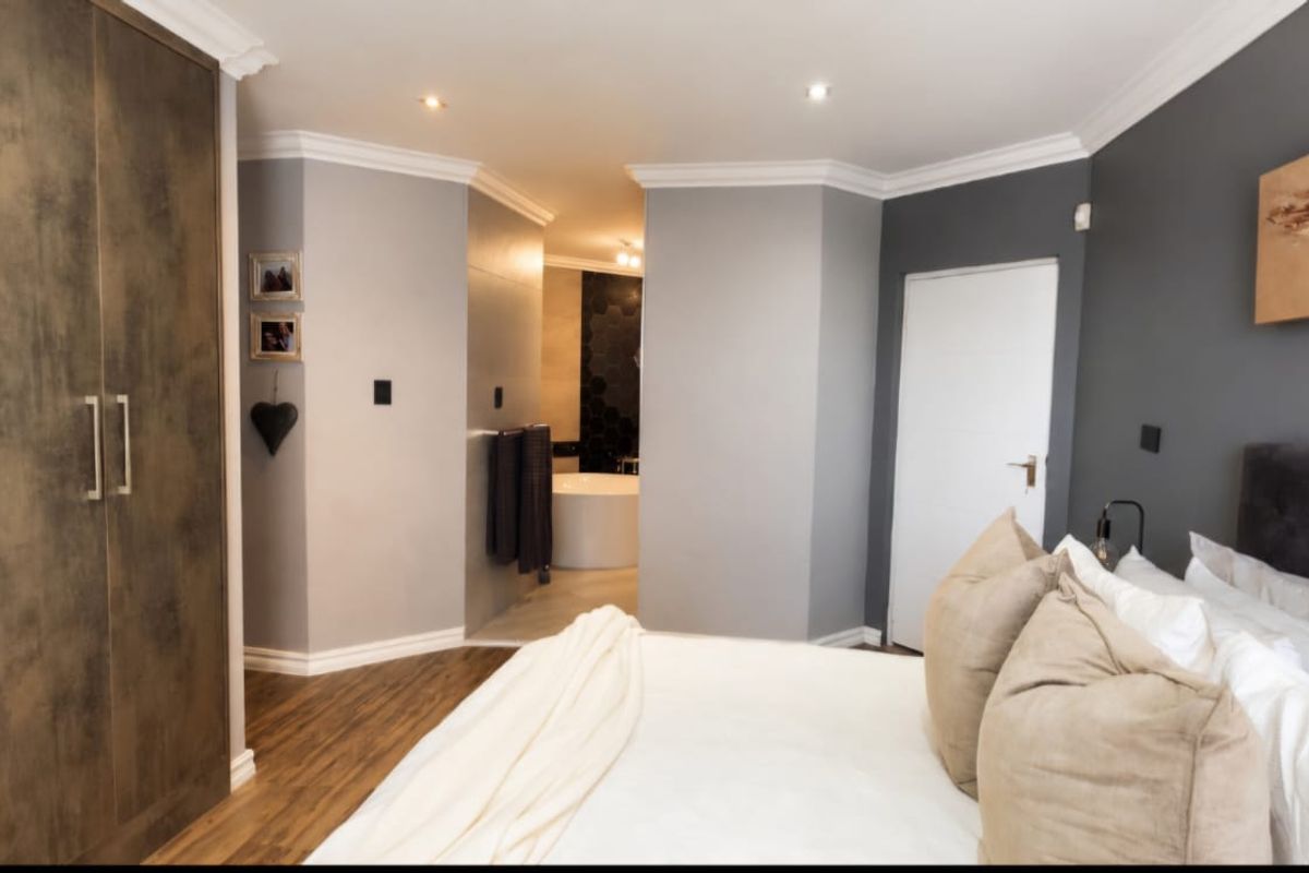 A well-appointed bedroom featuring built-in wardrobes, modern laminate flooring, and crown molding, with an open-plan transition to an en-suite bathroom area.