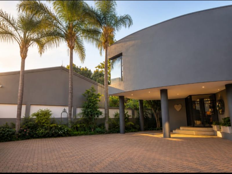 Modern front facade featuring a spacious paved driveway, structural columns, and well-maintained landscaping with mature palm trees.
