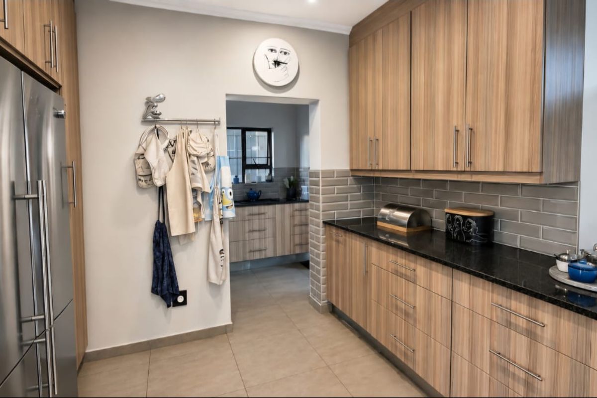 Modern kitchen featuring wood-grain cabinetry, granite countertops, and a subway tile backsplash, with an adjacent scullery area visible through the doorway.
