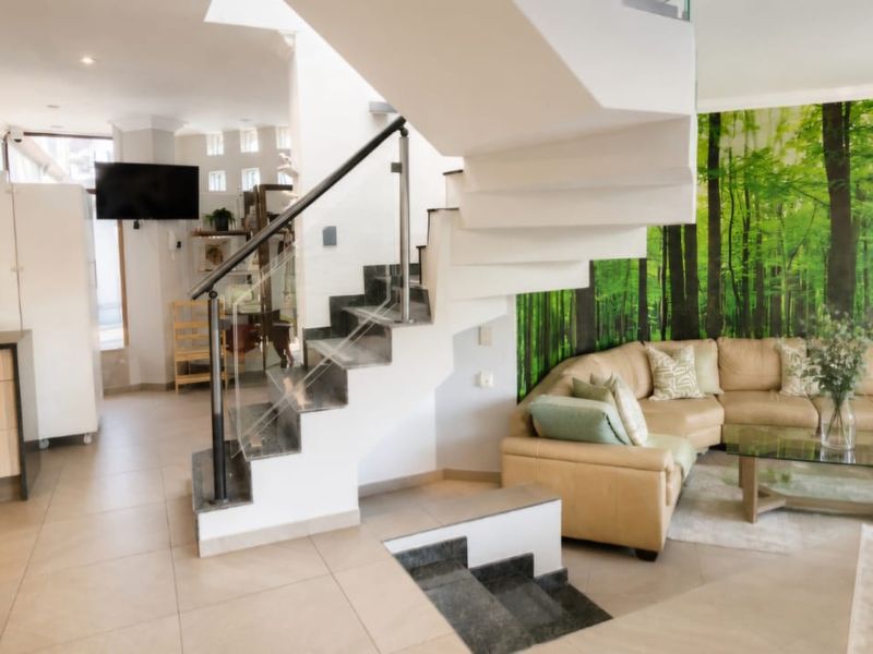 Modern open-plan living area featuring a striking floating staircase with glass balustrade, integrated kitchen cabinetry, and neutral tiled flooring throughout.