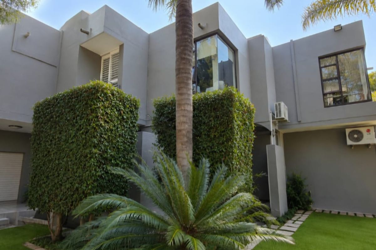 A modern double-story residential exterior featuring a grey facade, manicured garden, paved pathways, and integrated garage access.