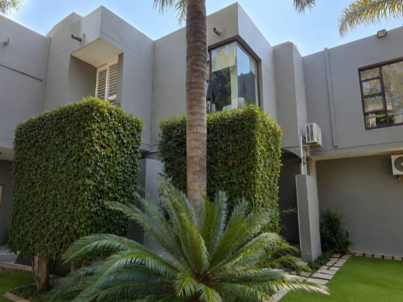 A modern double-story residential exterior featuring a grey facade, manicured garden, paved pathways, and integrated garage access.
