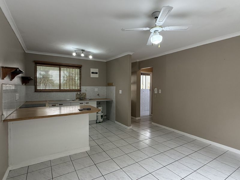 Open-plan living and kitchen area featuring tiled flooring, a ceiling fan, and functional kitchen cabinetry with a breakfast bar.