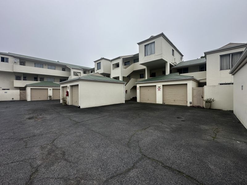 Exterior view of an apartment complex featuring multiple garage units, an asphalt driveway, and external staircases providing access to upper-level residential units.